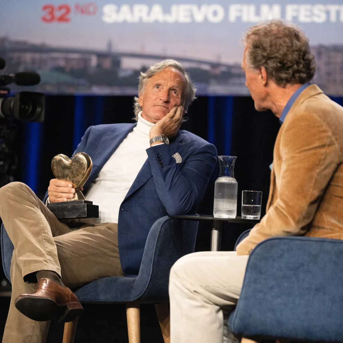 Woody Harrelson seated on stage at the 32nd Sarajevo Film Festival, holding his Honorary Heart of Sarajevo award while in conversation.