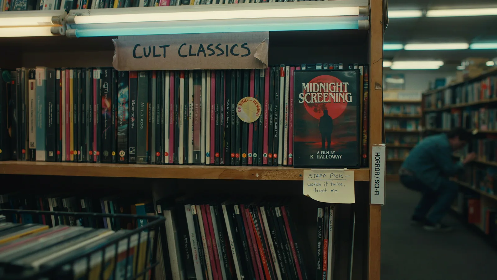 A video rental store shelf labeled Cult Classics with a fictional Midnight Screening DVD and a staff pick note reading watch it twice, trust me.