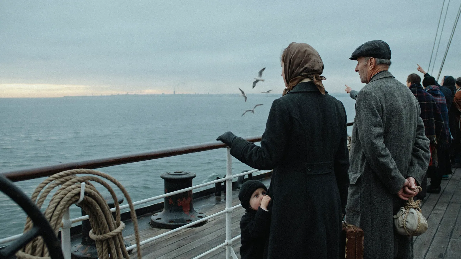 A worn suitcase and passport resting on an airport bench beside a family silhouette, titled Best Movies About Immigration.
