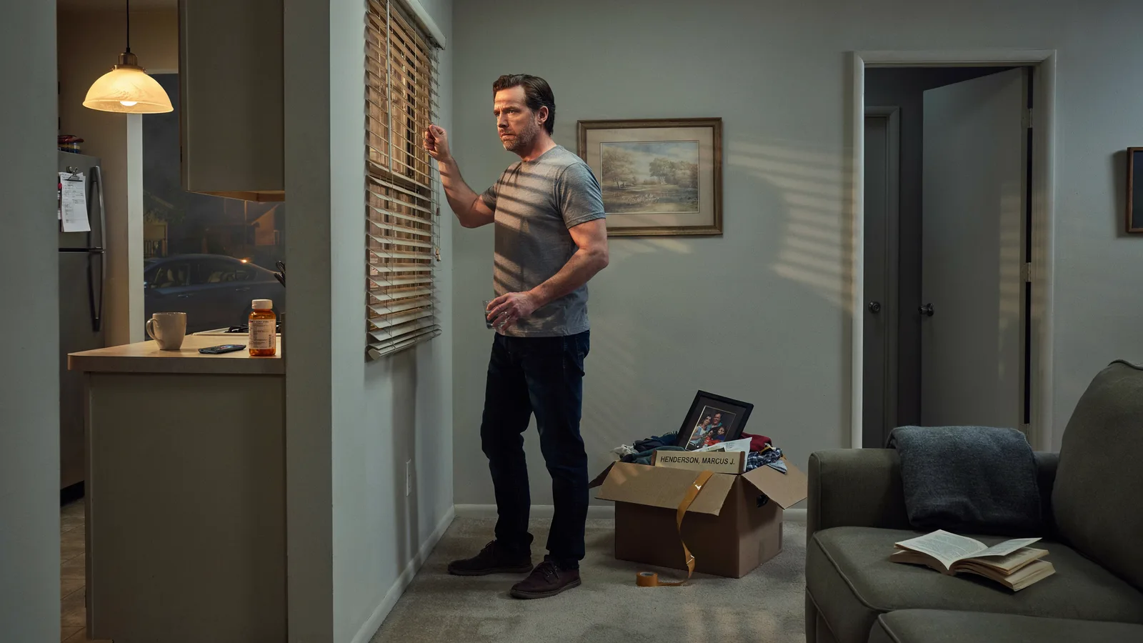 A man peering through blinds beside a half-packed moving box labeled with a new name, titled Best Series About Witness Protection.
